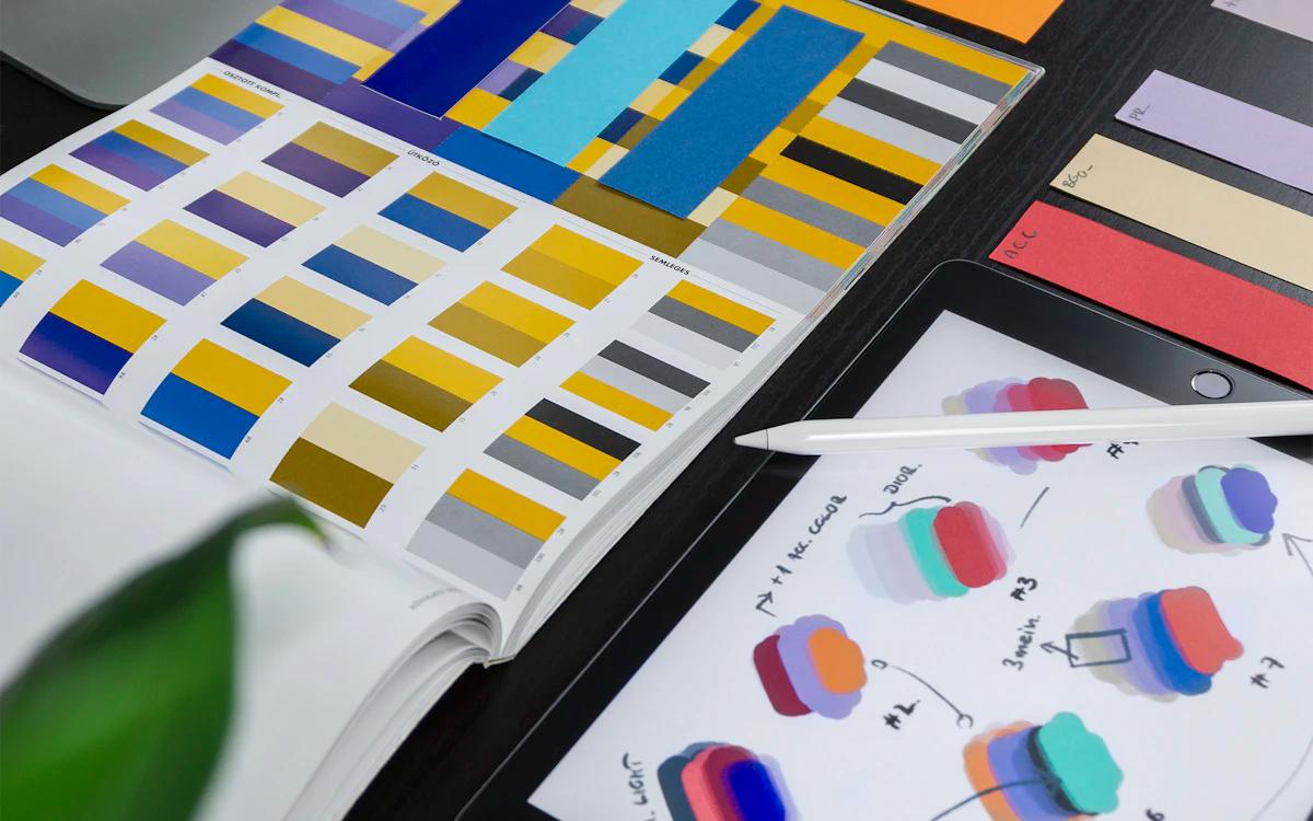 Colour-palette swatch booklet beside a tablet with design sketches